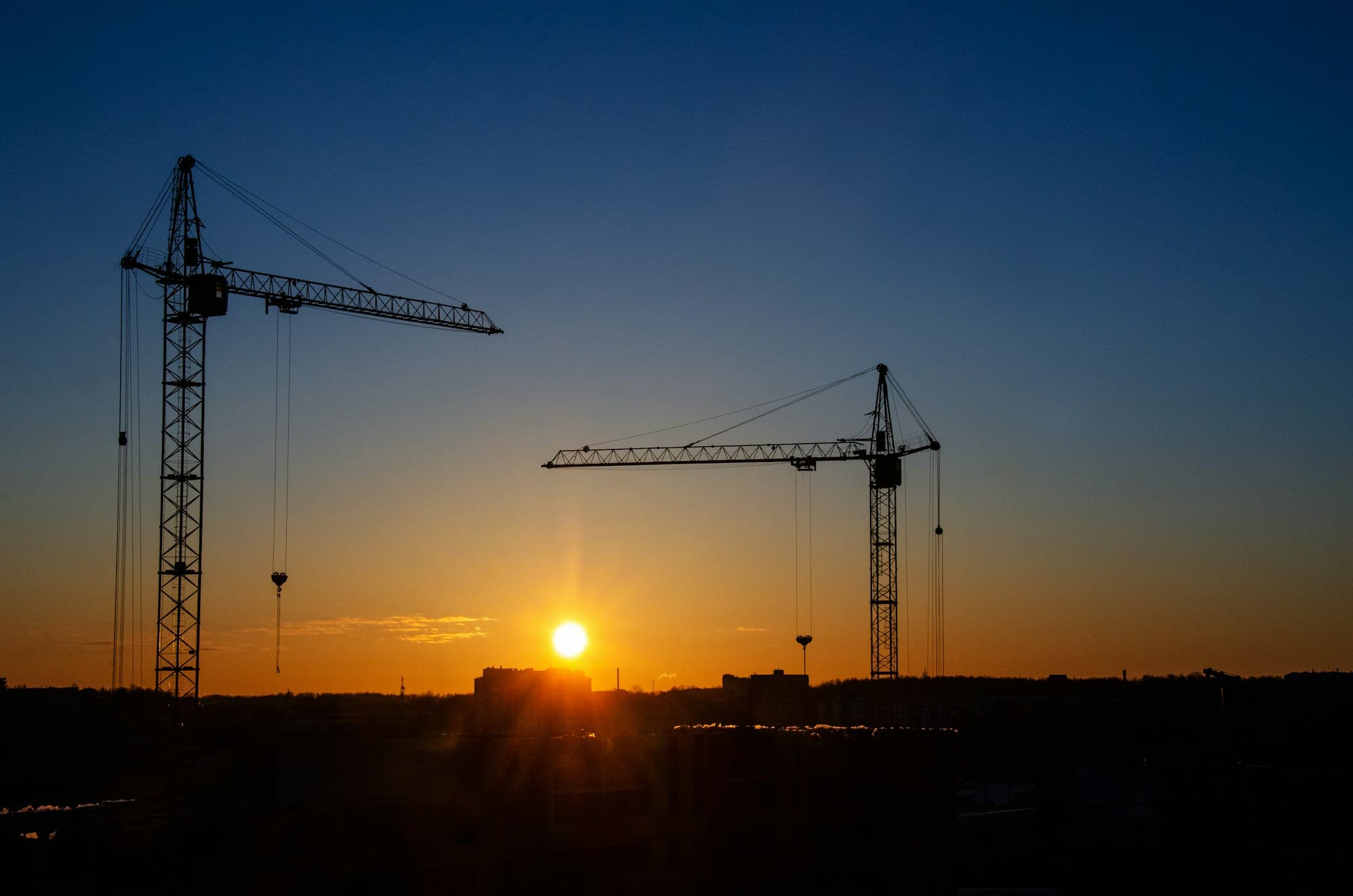Deux grues de chantier en silhouette au lever du soleil.